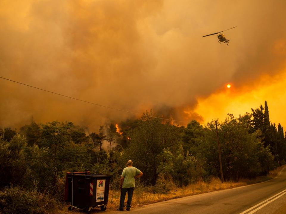 A man watches a helicopter during a fire in the village of Villa, northwestern Athens (AFP via Getty Images)