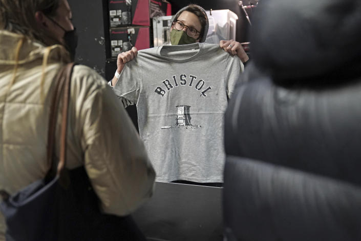 A person inside Rough Trade in Bristol, England, Saturday Dec. 11, 2021, holds up a T-shirt designed by street artist Banksy, being sold to support four people facing trial accused of criminal damage in relation to the toppling of a statue of slave trader Edward Colston. The anonymous artist posted on Instagram pictures of limited edition grey souvenir T-shirts which will go on sale on Saturday in Bristol. The shirts have a picture of Colston's empty plinth with a rope hanging off, with debris and a discarded sign nearby. (Jacob King/PA via AP)