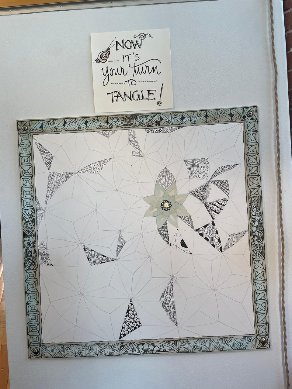 Those who view the exhibit can try their own Zentangle design, as some have done already, using this framed board that is hanging on the wall. Zentangle co-founder Maria Thomas created the lettering and the board.