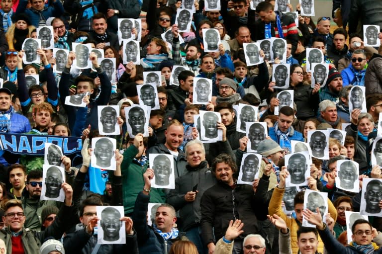 People hold flyers depicting the face of Napoli's defender Kalidou Koulibaly before an Italian Serie A football match against Carpi FC on February 7, 2016 at the San Paolo stadium in Naples