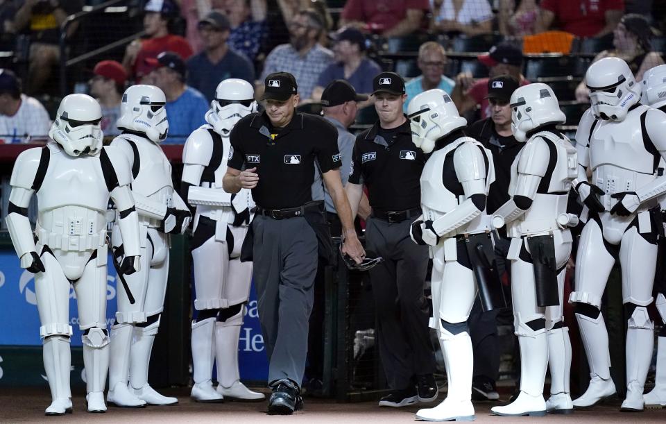 Umpires Andy Fletcher, left, and Junior Valentine are flanked by "Star Wars" stormtroopers as they walk on the field during Star Wars night, prior to a baseball game between the Arizona Diamondbacks and the Washington Nationals on Saturday, July 23, 2022, in Phoenix. (AP Photo/Ross D. Franklin)