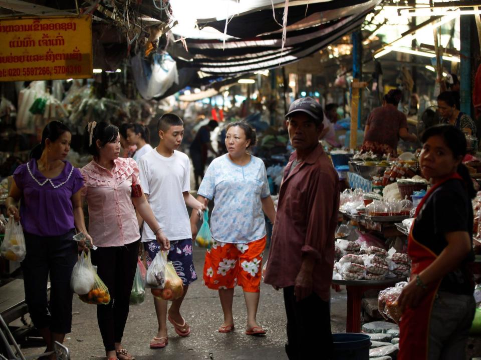 Shoppers, some carrying goods in plastic bags, walk through a local market selling fresh goods under awnings in downtown Vientiane, Laos, Sunday, Nov. 4, 2012.