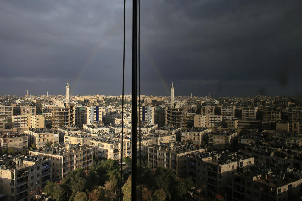 FILE - In this Dec. 3, 2016 file photo a rainbow appears over residential buildings after a heavy rain over Aleppo, Syria. A new Syrian law empowering the government to confiscate property is threatening to leave refugees stuck in Europe with no homes to return to. (AP Photo/Hassan Ammar, file)