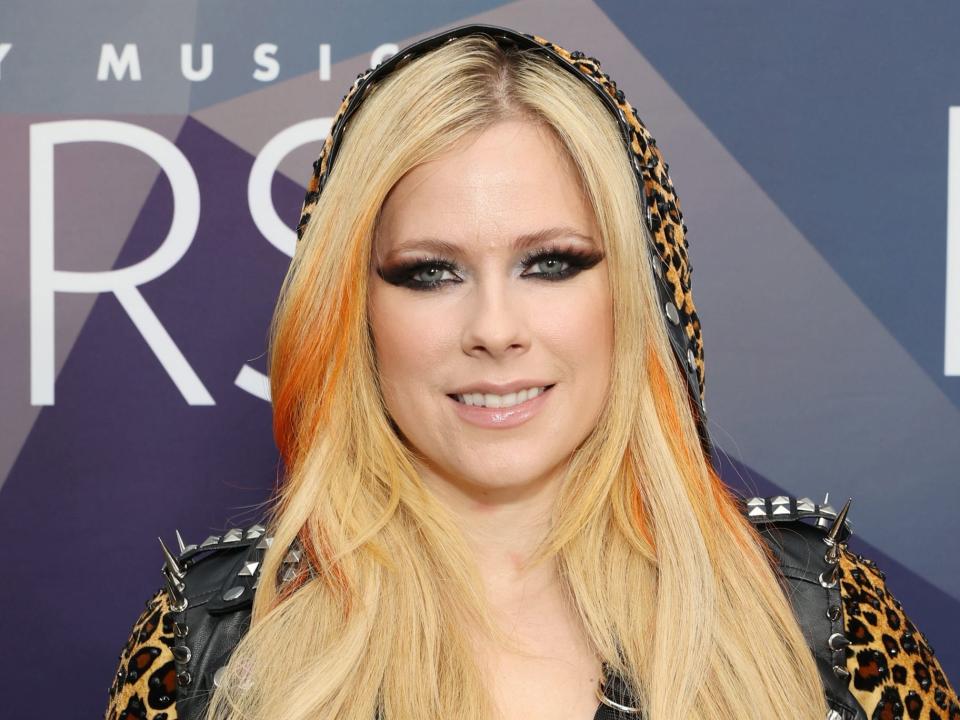 Avril Lavigne poses on the red carpet in a leopard-pring hoodie and a leather vest.