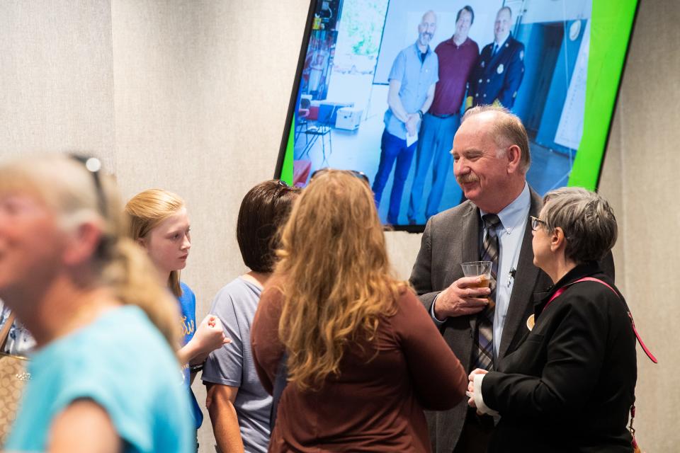 People mingle as a slideshow displays photos of Mark Watson during his retirement reception. Standing in front of the screen is Deputy City Manager Jack Suggs who will serve as interim until a new city manager is hired.