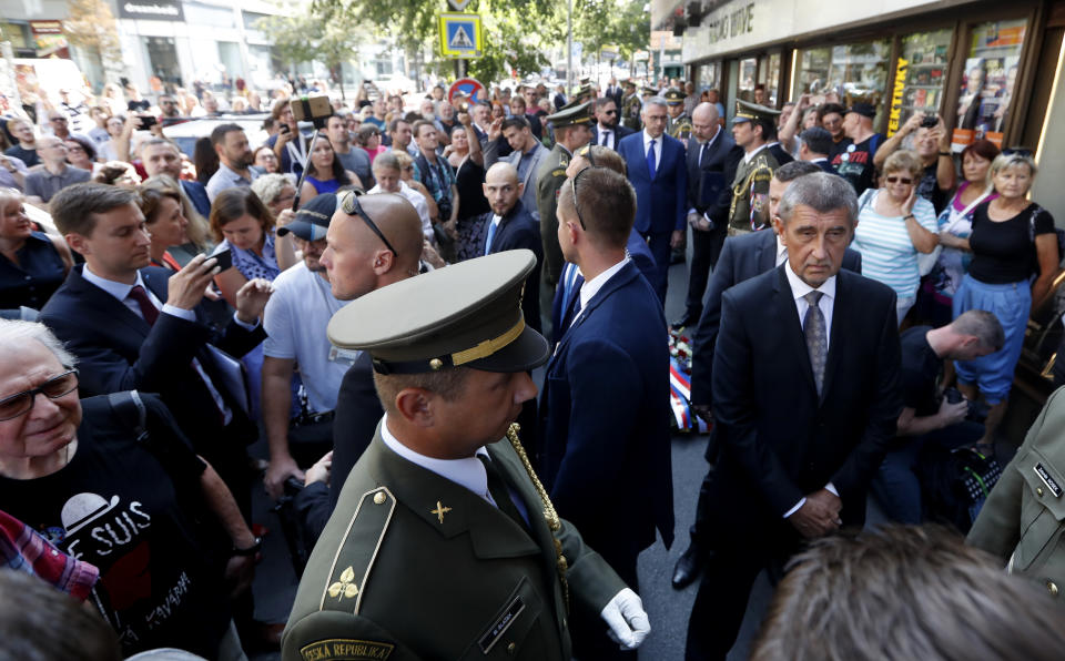 Czech Republic's Prime Minister Andrej Babis, front right, arrives to lay a wreath of flowers to honor the victims of the Soviet-led invasion of Czechoslovakia in 1968 at a ceremony in Prague, Czech Republic, Tuesday, Aug. 21, 2018. Dozens of protesters gathered to oppose the prime minister. Babis, a populist billionaire, is a controversial figure for many due to a power-sharing deal with the maverick Communist Party and fraud charges he is facing. His position is also complicated by allegations he collaborated with the former communist-era secret police. The white banner reads: "Babis is a liar". (AP Photo/Petr David Josek)