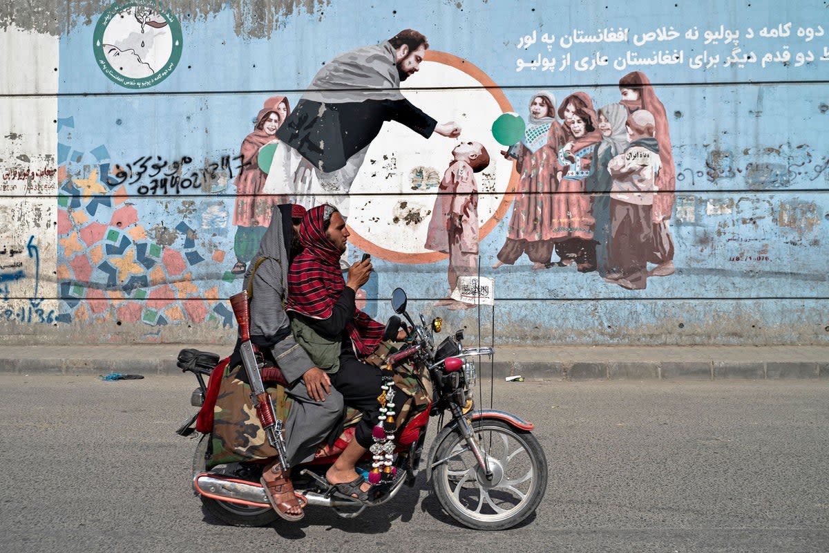 Taliban security personnel ride a motorcycle past a mural depicting polio vaccination campaign in Kabul (AFP via Getty Images)