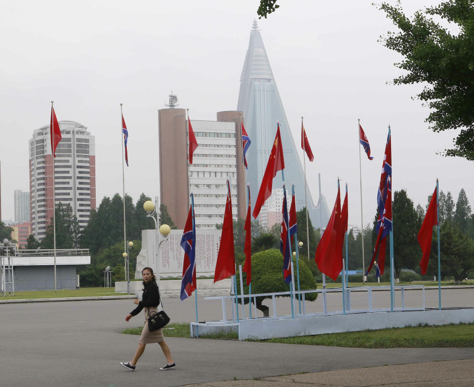 A woman walks past North Korean and Chinese national flags hoisted on a street in Pyongyang, North Korea Thursday, June 20, 2019. Chinese President Xi Jinping arrived Thursday morning for a two-day state visit to North Korea, where he is expected to talk with leader Kim Jong Un about the stalled negotiations with Washington over North Korea's nuclear weapons. (AP Photo/Jon Chol Jin)