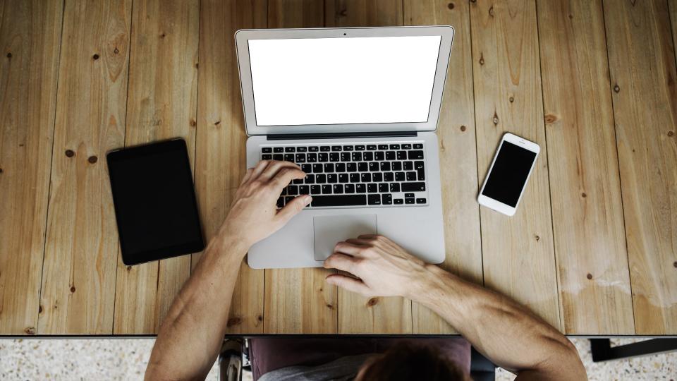 Man at wooden desk with tablet, laptop and smartphone