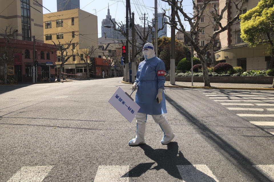 A worker in protective gear holds a sign which reads "Keep one meter apart" along an empty street in a lockdown area in the Jingan district of western Shanghai, Monday, April 4, 2022. China has sent more than 10,000 health workers from across the country to Shanghai, including 2,000 military medical staff, as it struggles to stamp out a rapidly spreading COVID-19 outbreak in China's largest city. (AP Photo/Chen Si)