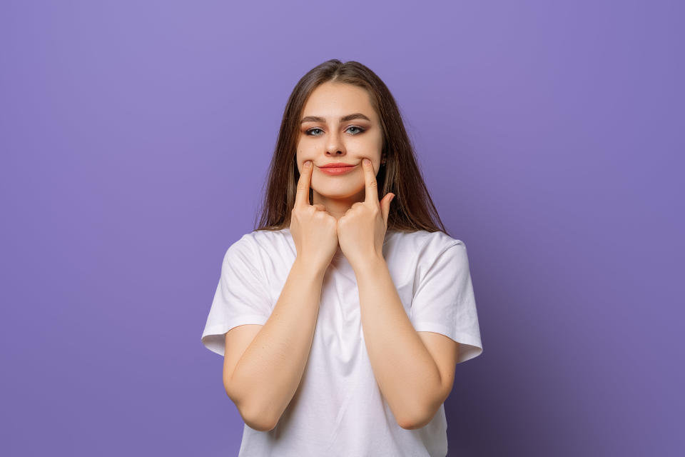 woman using her fingers to stretch her mouth into a smile