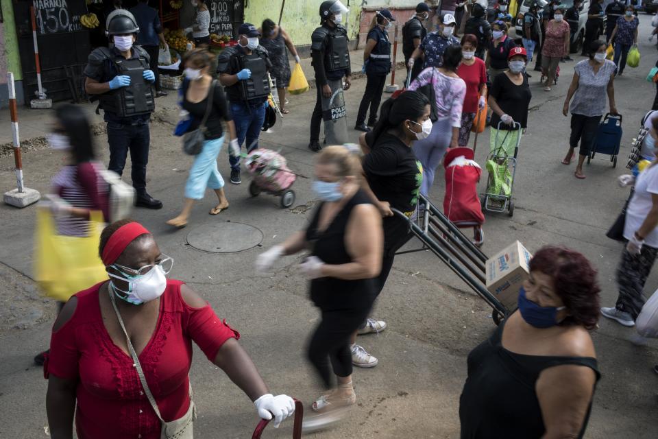 Police stand guard as women, wearing protective face masks shop at a popular market in Lima, Peru, Saturday, April 4, 2020. Due to the health emergency from the spread of the new coronavirus, the government is restricting people's movement by gender, with Saturday designated for women, who can leave home to buy basic necessities. (AP Photo/Rodrigo Abd)