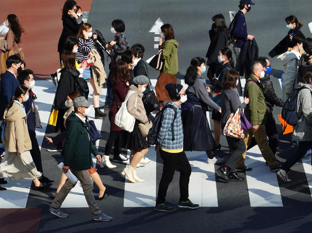 People wearing protective masks to help curb the spread of the coronavirus walk at a pedestrian crossing in Tokyo (AP/Eugene Hoshiko)