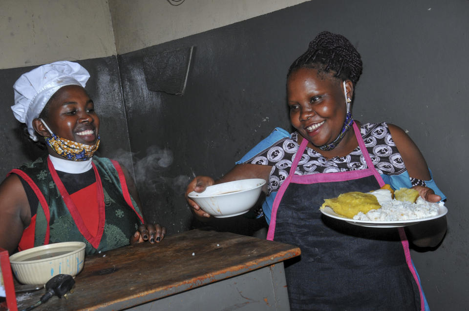 In this photo taken Saturday, June 20, 2020, Rebecca Nakamanya, left, and colleague Namara Grace, right, work at a restaurant near a bus terminal in capital Kampala, Uganda. The COVID-19 pandemic means that millions of women in Africa and other developing regions could lose years of success in contributing to household incomes, asserting their independence and expanding financial inclusion. (AP Photo/Ronald Kabuubi)