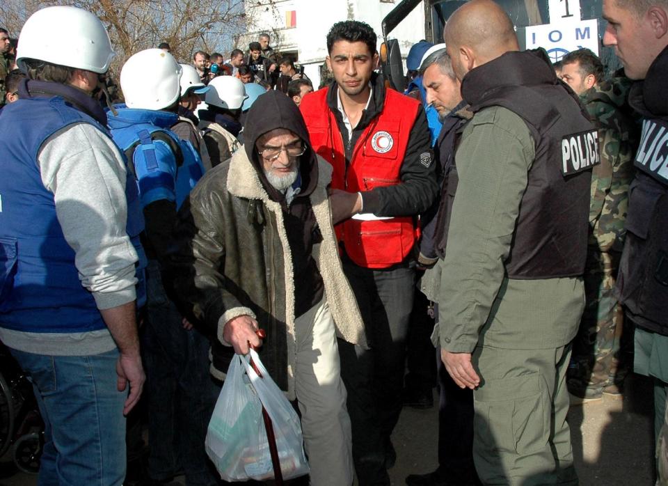 In this taken on Sunday Feb. 9, 2014 file photo, released by the Syrian official news agency SANA, a Syrian Arab Red Crescent member in red uniform helps a man, as Syrian security forces, right, look at him as he walks to a bus to evacuate the battleground city of Homs, Syria. Weeping children begged for food in the streets and women picked grass growing in the cracks of the sidewalks to eat as hunger gripped residents of rebel-held neighborhoods of the Syrian city of Homs blockaded for nearly two years by the Syrian military, according to a rare first-hand account by a man evacuated during a truce this week. (AP Photo/SANA, File)