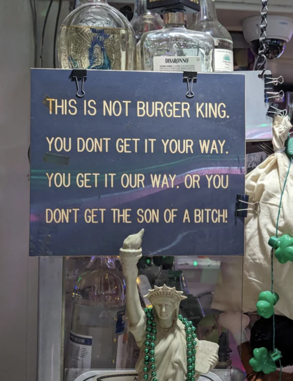 Sign reads "This is not Burger King. You don't get it your way. You get it our way or you don't get the son of a bitch!" surrounded by bottles and decor