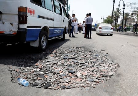 Policemen and people walk on a cracked road in front of the damaged facade of the National Cancer Institute, after an overnight fire from a blast, in Cairo