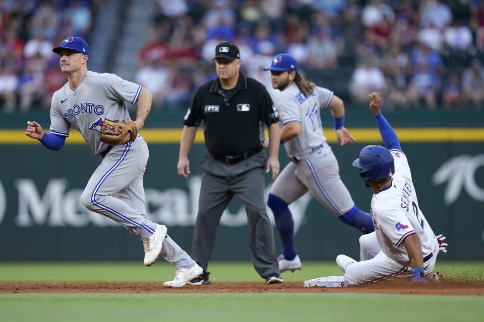 Texas Rangers' Marcus Semien (2) steals second base as Toronto Blue Jays' Matt Chapman, left, and Bo Bichette, rear, move to cover third base as umpire Todd Tichenor, second from left, looks on in the first inning of baseball game in Arlington, Texas, Saturday, Sept. 10, 2022. (AP Photo/Tony Gutierrez)