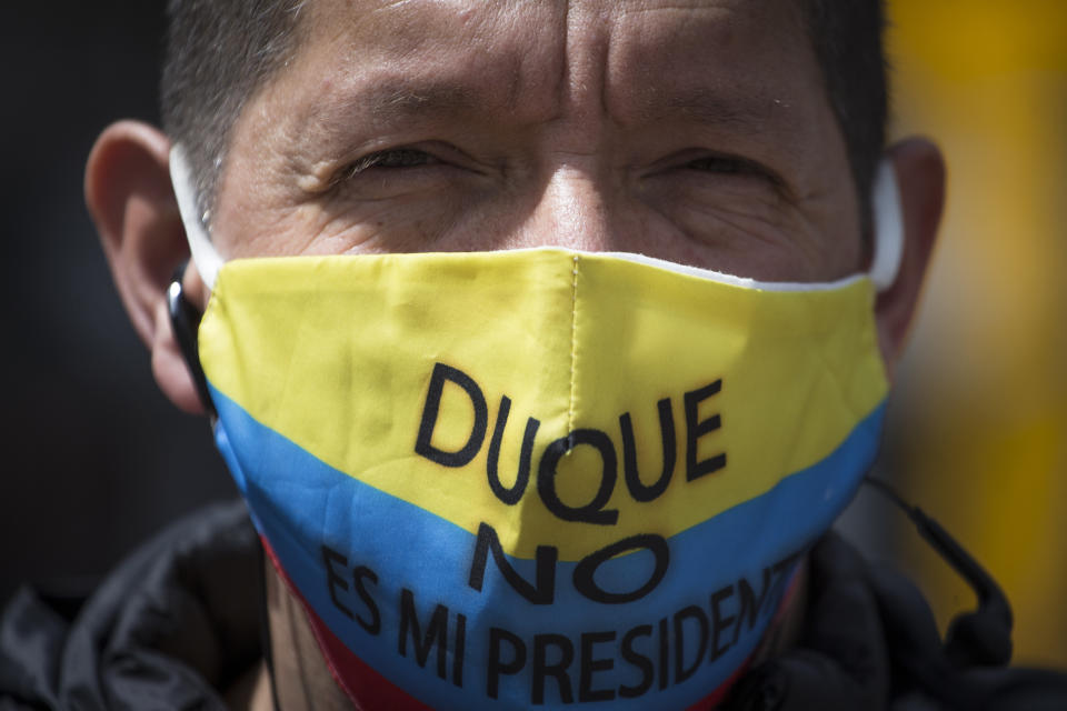 A protester wears a mask with the Colombian flag colors and Spanish message "Duque isn't my president," referring to President Iván Duque, during the march toward the residence of Bogota Mayor Claudia López to demand the lifting of the city-wide curfew and the reopening of business amid the COVID-19 pandemic in Bogota, Colombia, Wednesday, Jan. 20, 2021. (AP Photo/Ivan Valencia)
