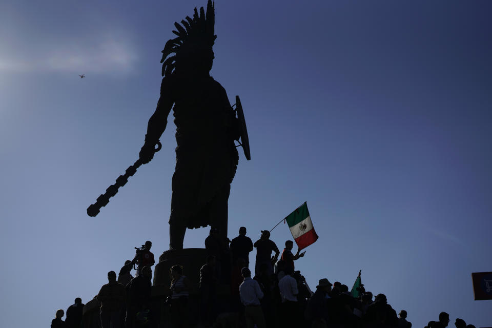 Demonstrators stand under an indigenous statue of Aztec ruler Cuauhtemoc as they protest the presence of thousands of Central American migrants in Tijuana, Mexico, Sunday, Nov. 18, 2018. Protesters accused the migrants of being messy, ungrateful and a danger to Tijuana; complained about how the caravan forced its way into Mexico, calling it an "invasion," and voiced worries that their taxes might be spent to care for the group as they wait possibly months to apply for U.S. asylum. (AP Photo/Ramon Espinosa)