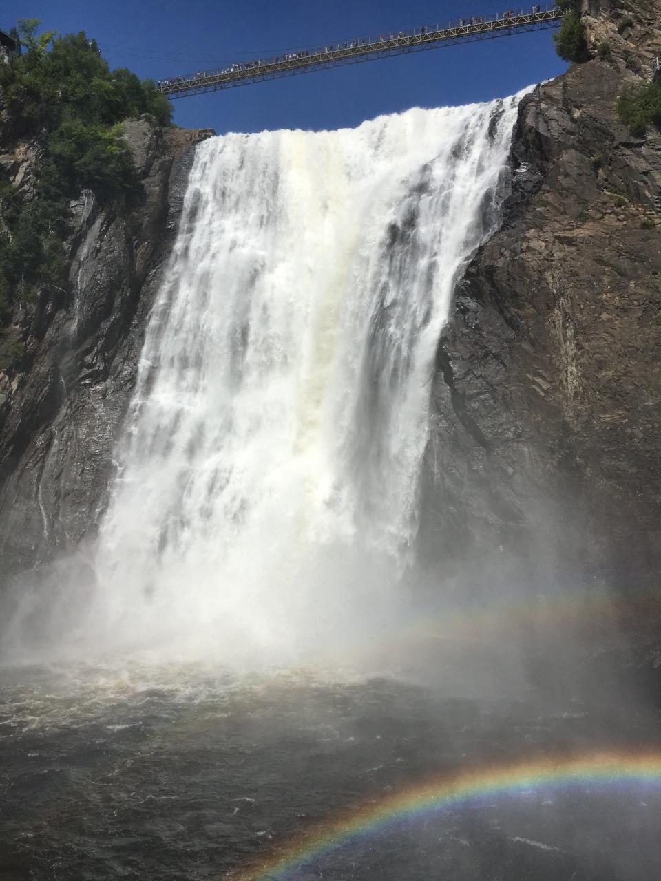 Montmorency Falls outside of downtown Quebec City. A pedestrian bridge crosses over top, and a rainbow shows in the bottom right.