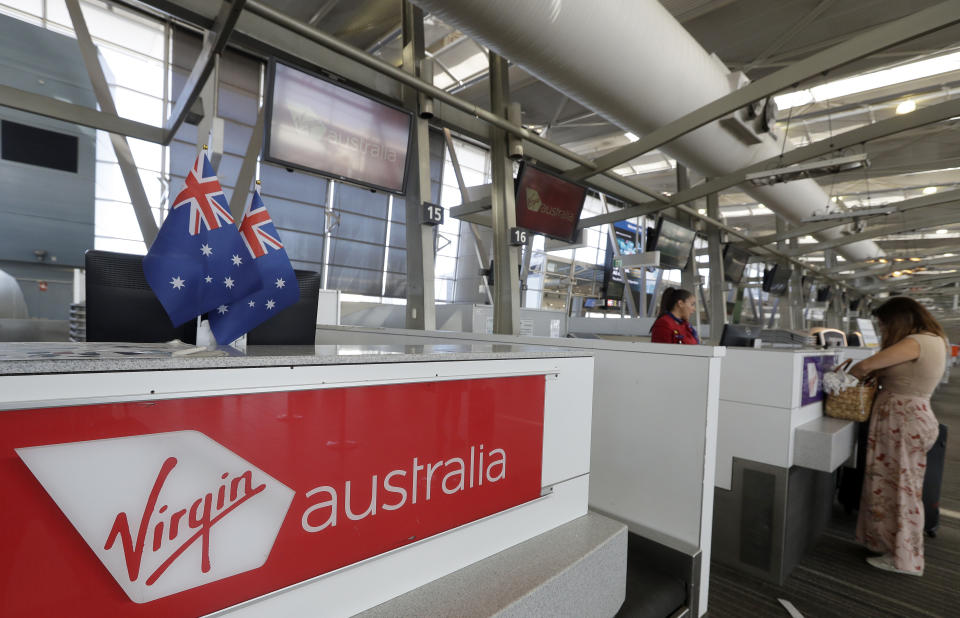 A Virgin Australia worker, left, helps a customer at the check-in counters at Sydney Airport in Sydney, Wednesday, April 22, 2020. Virgin Australia is seeking bankruptcy protection, entering voluntary administration after a debt crisis worsened by the coronavirus shutdown pushed it into insolvency. (AP Photo/Rick Rycroft)