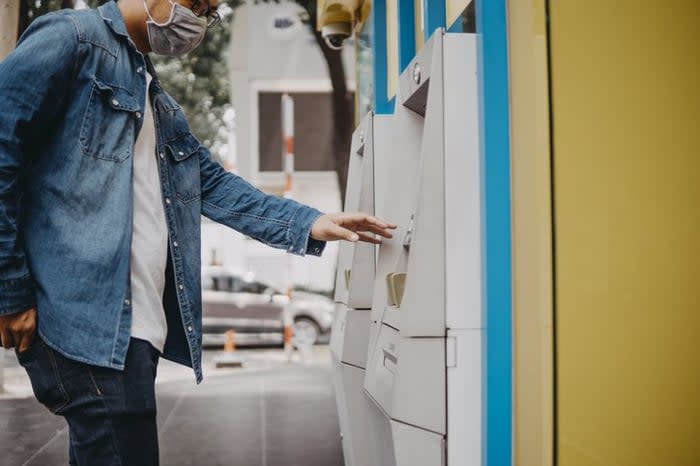 A man wearing a medical mask and taking money out of an ATM on the street.