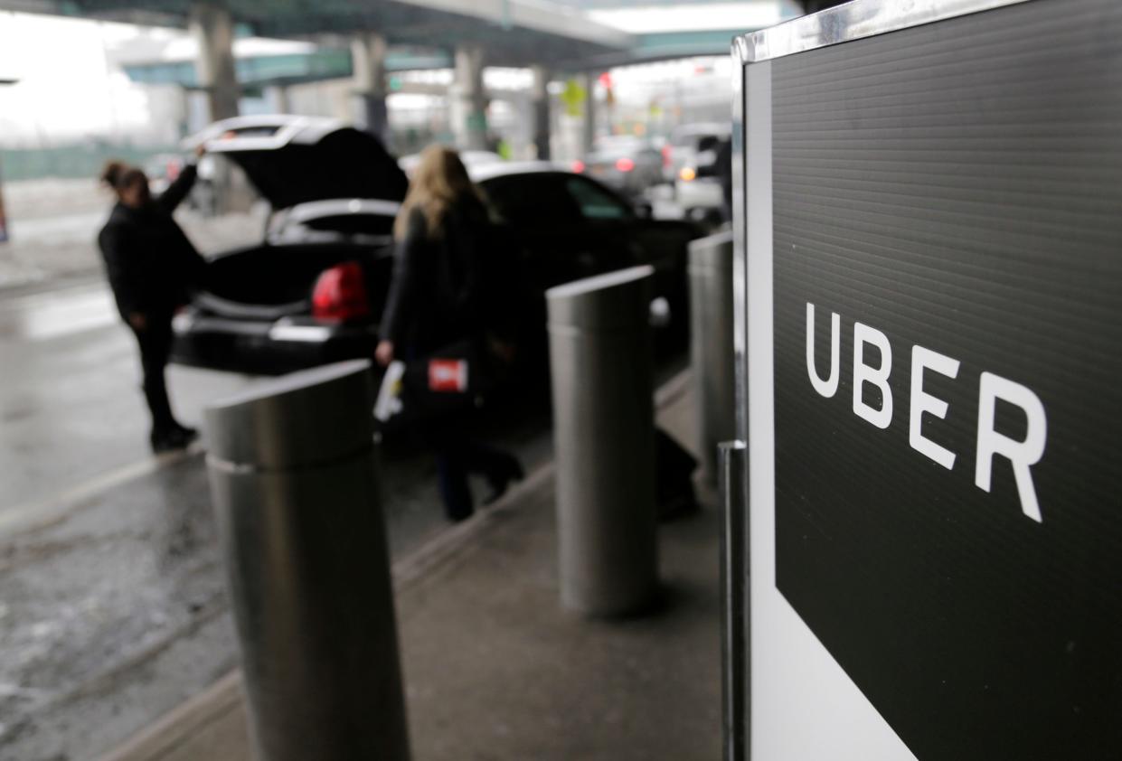 Two people standing next to an Uber sign while they load bags into the trunk of a car.