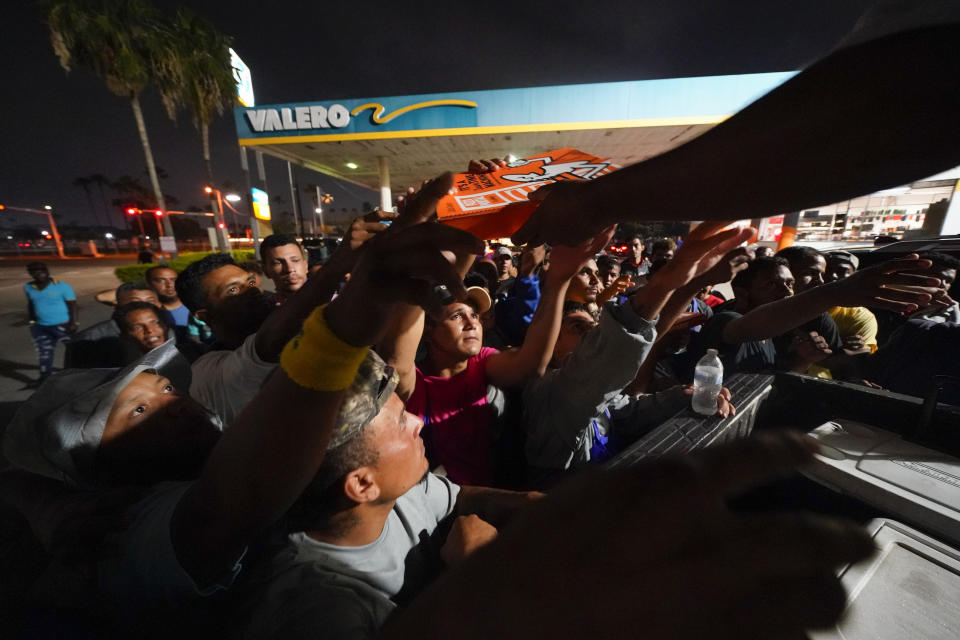 Migrantes reciben pizza de voluntarios tras ser liberados de un centro de refugio en la frontera entre Texas y México, el jueves 11 de mayo de 2023, en Brownsville, Texas. (AP Foto/Julio Cortez)