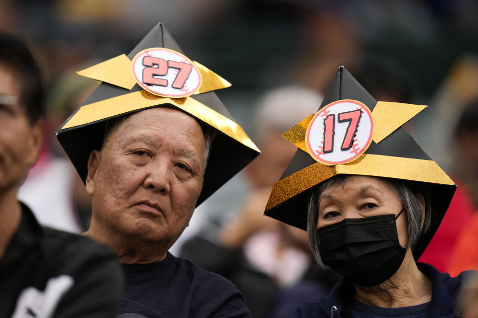 Two fans wear paper helmets in the shape of kabuto at a baseball game between the Los Angeles Angels and the Chicago Cubs on Tuesday, June 6, 2023, in Anaheim, Calif. (AP Photo/Jae C. Hong)
