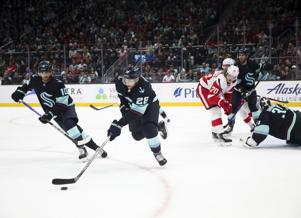 Seattle Kraken defenseman Carson Soucy (28) moves the puck away from the Kraken goal as Detroit Red Wings center Oskar Sundqvist (70) watches during the first period of an NHL hockey game Saturday, Feb. 18, 2023, in Seattle. (AP Photo/ Lindsey Wasson)