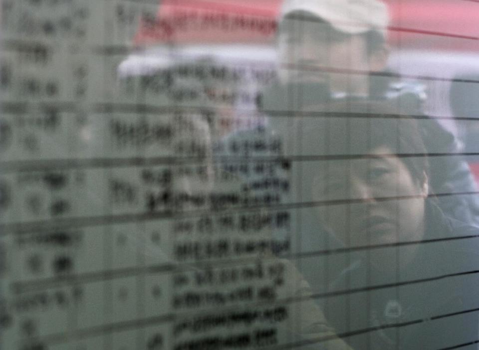 Relatives of passengers aboard the sunken ferry Sewol are reflected on a board of the official list of the dead victims at a port in Jindo, South Korea, Monday, April 21, 2014. Divers continued the grim work of recovering bodies from inside the sunken South Korean ferry in the water off the southern coast Monday, as a newly released transcript showed the ship was crippled by confusion and indecision well after it began listing. The transcript suggests that the chaos may have added to a death toll that could eventually exceed 300. (AP Photo/Ahn Young-joon)