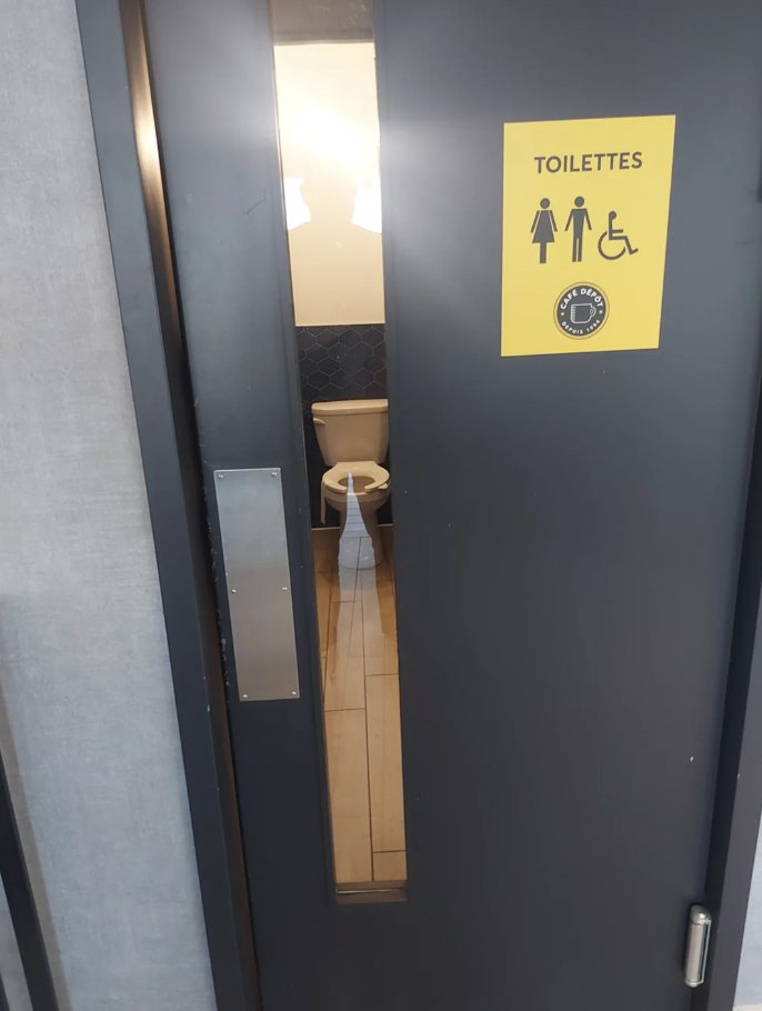 Public restroom door with a window in it that shows the toilet to anyone outside