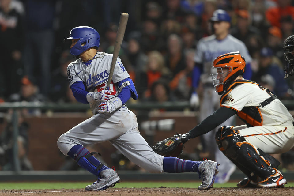 Los Angeles Dodgers' Mookie Betts, left, hits a single in front of San Francisco Giants catcher Buster Posey during the eighth inning of Game 5 of a baseball National League Division Series Thursday, Oct. 14, 2021, in San Francisco. (AP Photo/John Hefti)