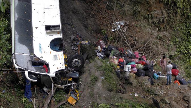 Warga berusaha mengambil barang-barang mereka dekat bus yang jatuh di jalan penghubung Medellin dan Bogota dekat San Luis, Provinsi Antiokia, Kolombia, 27 Desember 2021. Tujuh orang, termasuk seorang wanita hamil, tewas dan 20 lainnya luka-luka ketika sebuah bus terjun ke jurang. (Fredy BUILES/AFP)