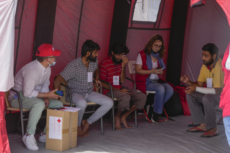Sobrevivientes del naufragio de un barco de arrastre que transportaba migrantes hablan con voluntarios de la Cruz Roja afuera de un almacén en el pueblo costero de Kalamata, Grecia, el jueves 15 de junio de 2023. (AP Foto/Thanassis Stavrakis)