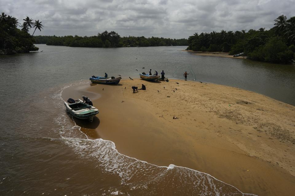 Fishing boats are docked as a man throws a fishing net by a sand dune in Iranawila, Sri Lanka, Monday, June 19, 2023. Much like the hundreds of other fishing hamlets that dot the coastline, the village of Iranawila suffers from coastal erosion. (AP Photo/Eranga Jayawardena)