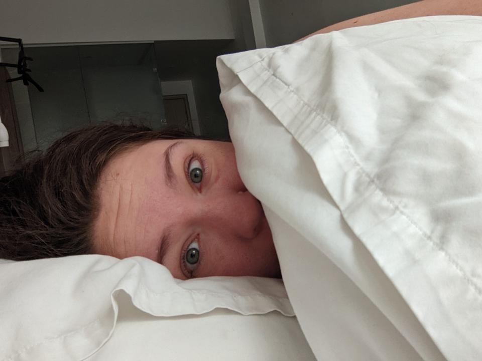 A woman lying in bed on a pillow with another pillow obscuring part of her face.