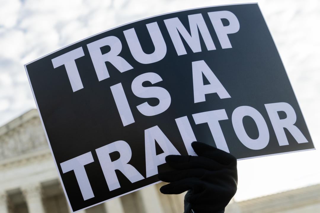 A protester holds a sign that reads, “Trump is a traitor.”