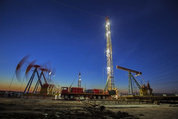 Oil pumps working the the background near a drilling rig at dusk.