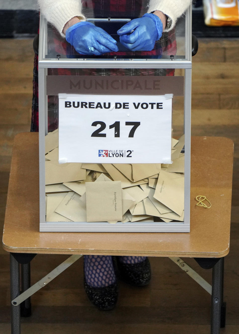 A volunteer using gloves waits for people in a polling station during local elections in Lyon, central France, Sunday, March 15, 2020. France is holding nationwide elections Sunday to choose all of its mayors and other local leaders despite a crackdown on public gatherings because of the new virus. For most people, the new coronavirus causes only mild or moderate symptoms. For some it can cause more severe illness. (AP Photo/Laurent Cipriani)