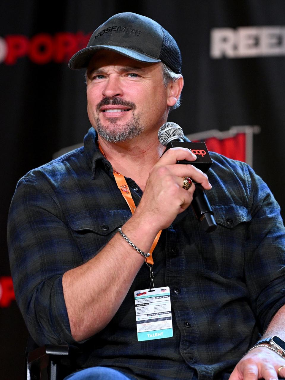 holding a mic on stage wearing a cap with a greying goatee