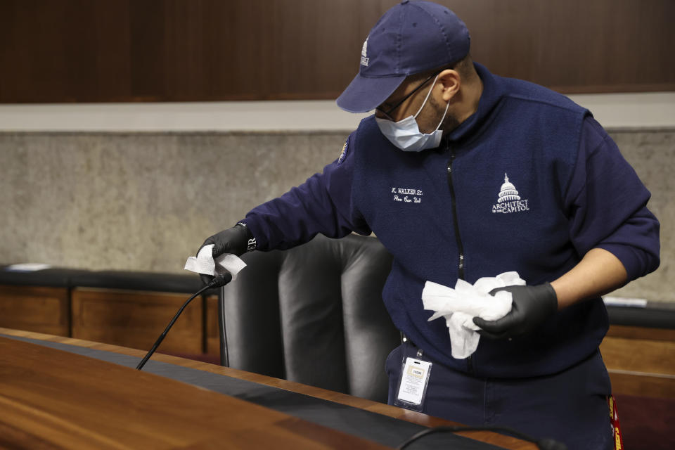 A worker wipes down microphone between Senate committee hearings in the Dirksen Senate Office Building on Capitol Hill during the coronavirus outbreak in Washington, Wednesday, May 6, 2020. (Jonathan Ernst/Pool Photo via AP)