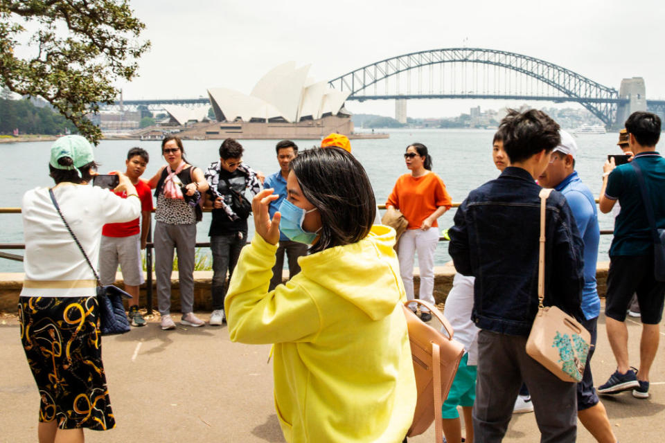 A woman in a yellow hoody walks past Mrs Macquarie's Chair in a face mask. 