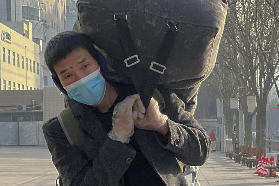 A migrant worker wearing a face mask and gloves carries his luggage as he arrived at the West Railway Station in Beijing, Friday, Jan. 6, 2023. China is seeking to minimize the possibility of a major new COVID-19 outbreak during this month's Lunar New Year travel rush following the end of most pandemic containment measures. (AP Photo/Wayne Zhang)