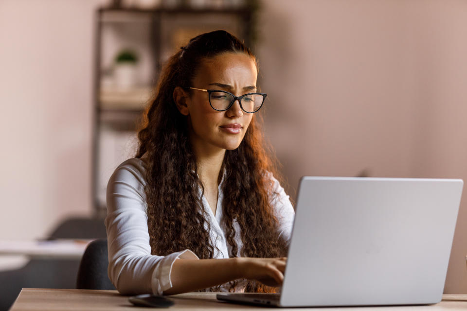 Portrait of serious young woman with eyeglasses frowning while using laptop at her desk.