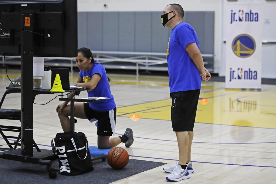 In this photo taken on Tuesday, June 9, 2020, Golden State Warriors basketball camp director Jeff Addiego, right, supervises coach Chanel Antonio as she speaks with her virtual students in Oakland, Calif. The Warriors had to adapt their popular youth basketball camps and make them virtual given the COVID-19 pandemic. (AP Photo/Ben Margot)
