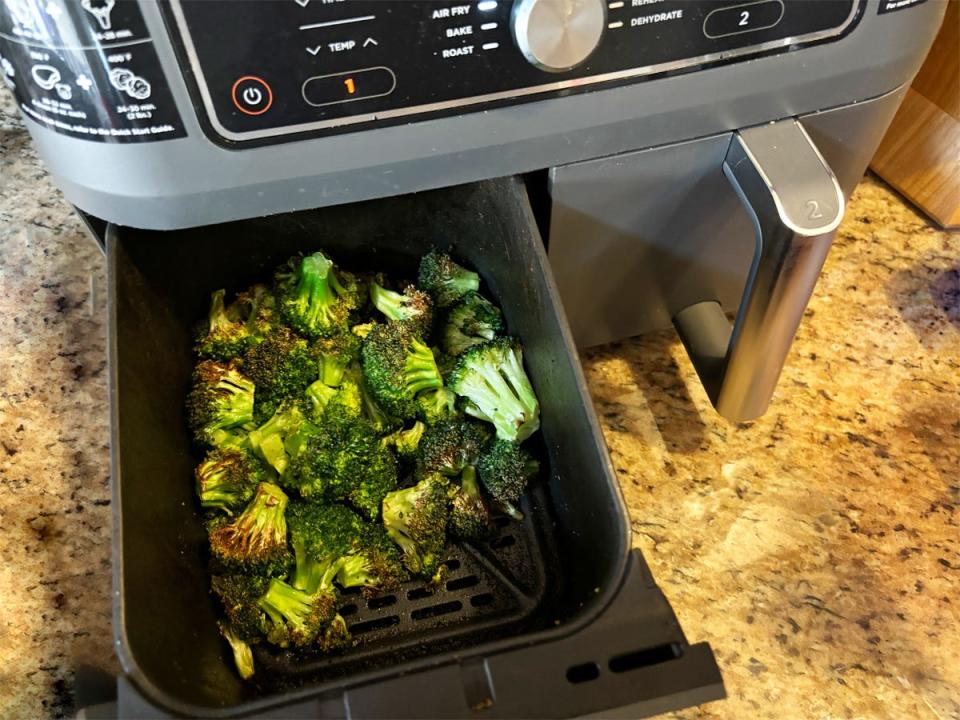 An open basket of the Ninja Foodi DualZone Air Fryer showing cooked broccoli.
