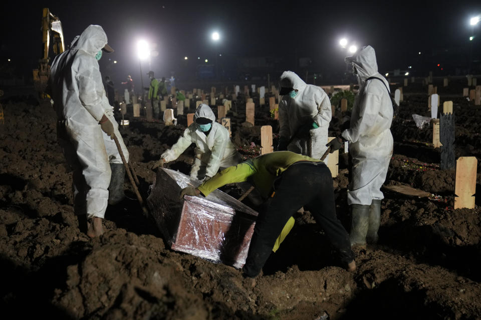 Workers bury a COVID-19 victim at Rorotan Cemetery in Jakarta, Indonesia, Thursday, July 1, 2021. New land around the capital city continues to be cleared for the dead and gravediggers have to work late shifts following surges in COVID-19 cases fueled by travel during the Eid holiday in May, and the spread of the delta variant of the coronavirus first found in India. (AP Photo/Dita Alangkara)