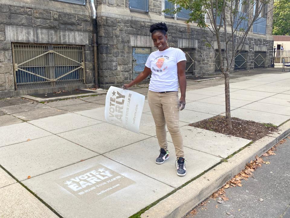 Activist Irize Earth is spray painting the floor with a stencil that reads “Vote early. Make your plan,” in Overbrook, west Philadelphia.Richard Hall / The Independent